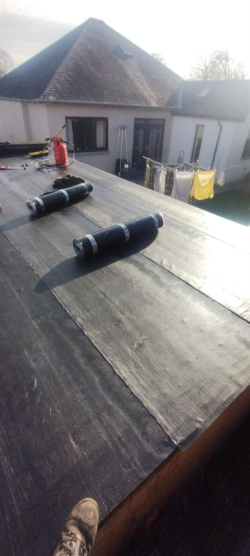 Torch-on felt going down — New membrane set out ready to bond, with upstands and edges dressed in as the work moves across.