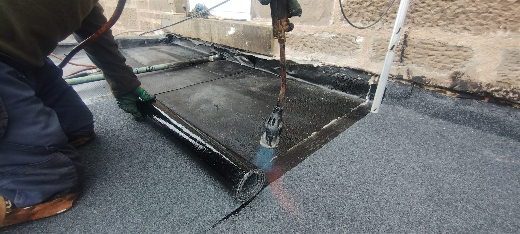 Torch-on felt being bonded down at a parapet upstand