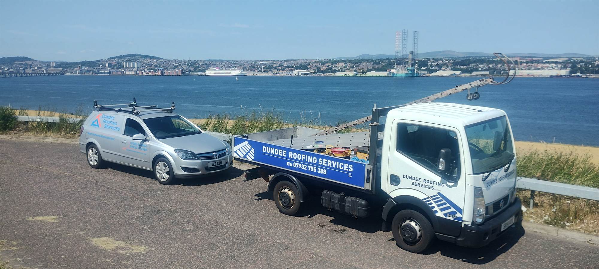 The Dundee Roofing Services truck and van parked above the Tay, with the Tay Road Bridge and the Dundee waterfront across the water behind them